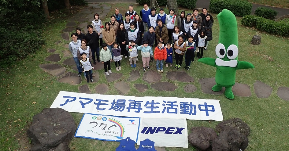 白と緑のアマモのマスコットと、それを笑顔で囲む人々。