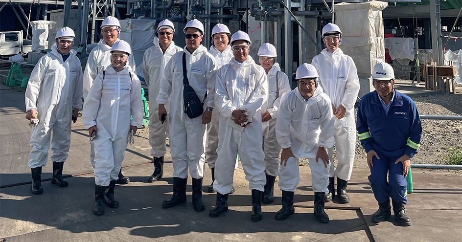 作業現場で、白いカバーオール、安全ヘルメット、手袋などの個人用保護具 (PPE) を着用した人々の集団。